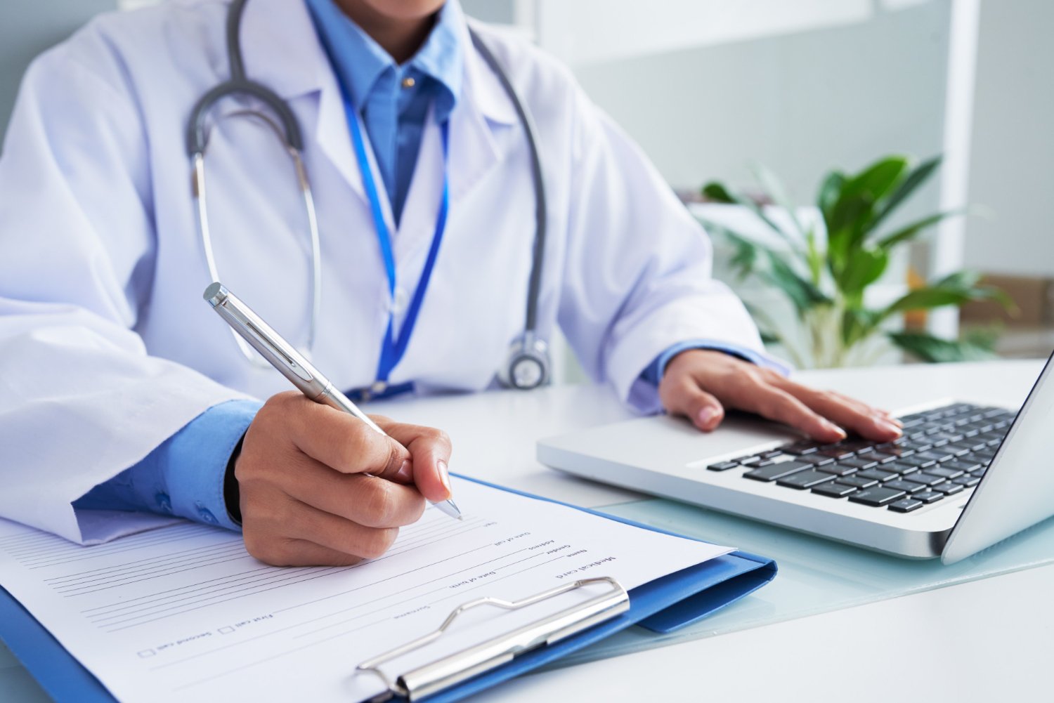 hands-of-unrecognizable-female-doctor-writing-on-form-and-typing-on-laptop-keyboard